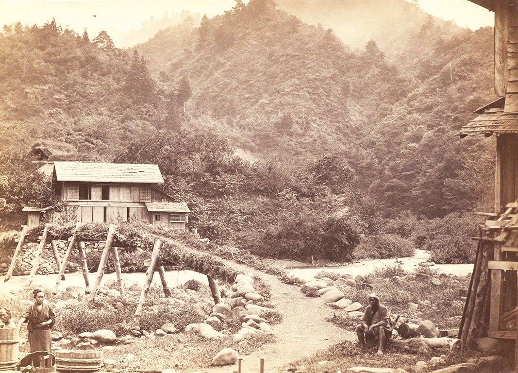 A wooden bridge with small house and montains in the background, people in the foreground