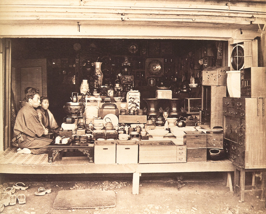 Two different people sitting in a different open-fronted shop