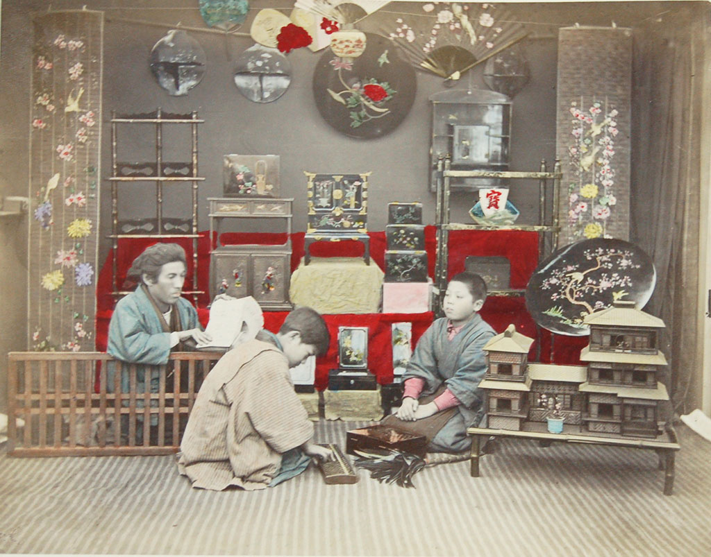 A man and two boys sittting amidst a colection of cabinets and shelves, doll house in the foreground