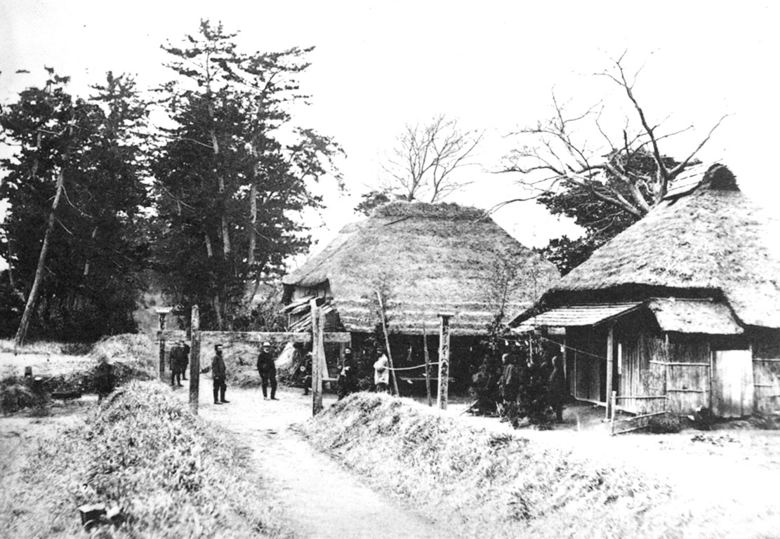 Village scene: huts, trees, a narrow road, people standing