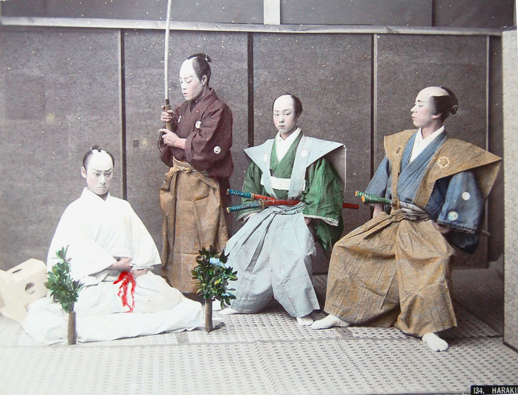 Tinted photograph, four men: on the left, a man kneeling; on the right, one man standing, holding a sword, two men seated