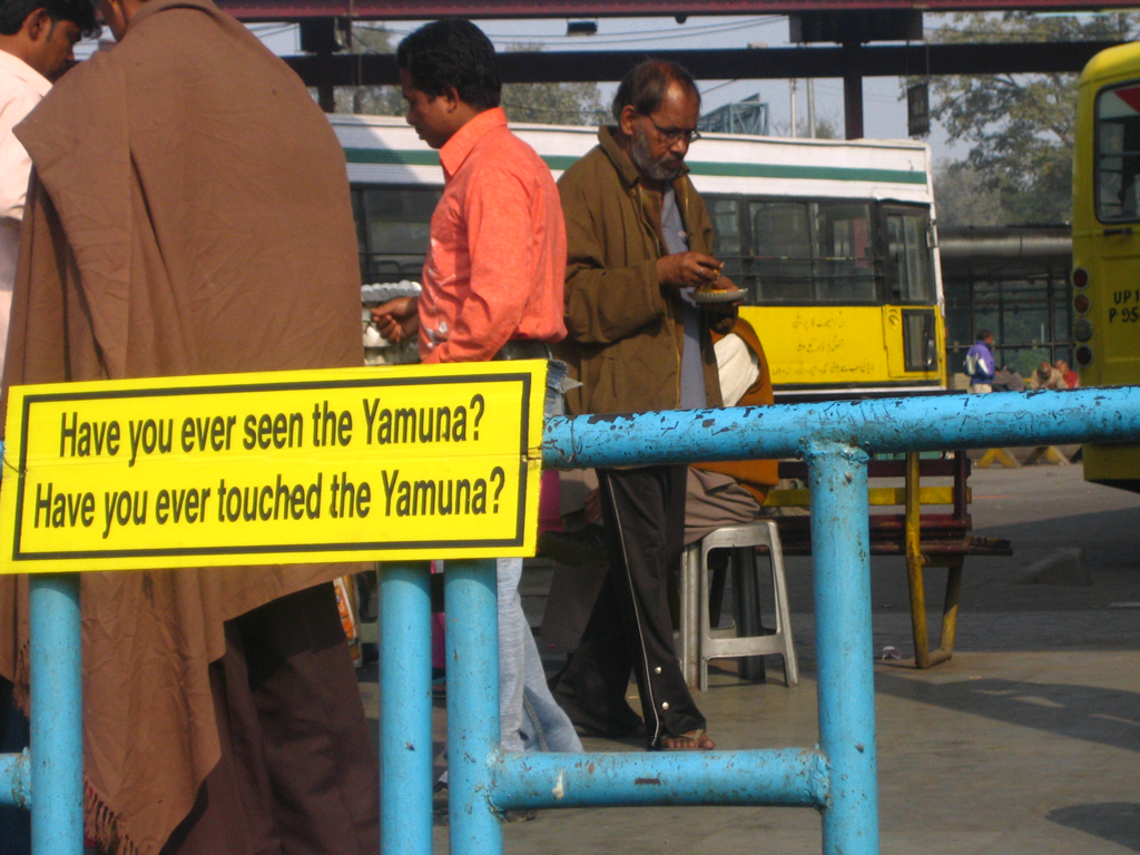 Street barrier with yellow sign: 'Have you ever seen the Yamuna? Have you ever touched the Yamuna?'