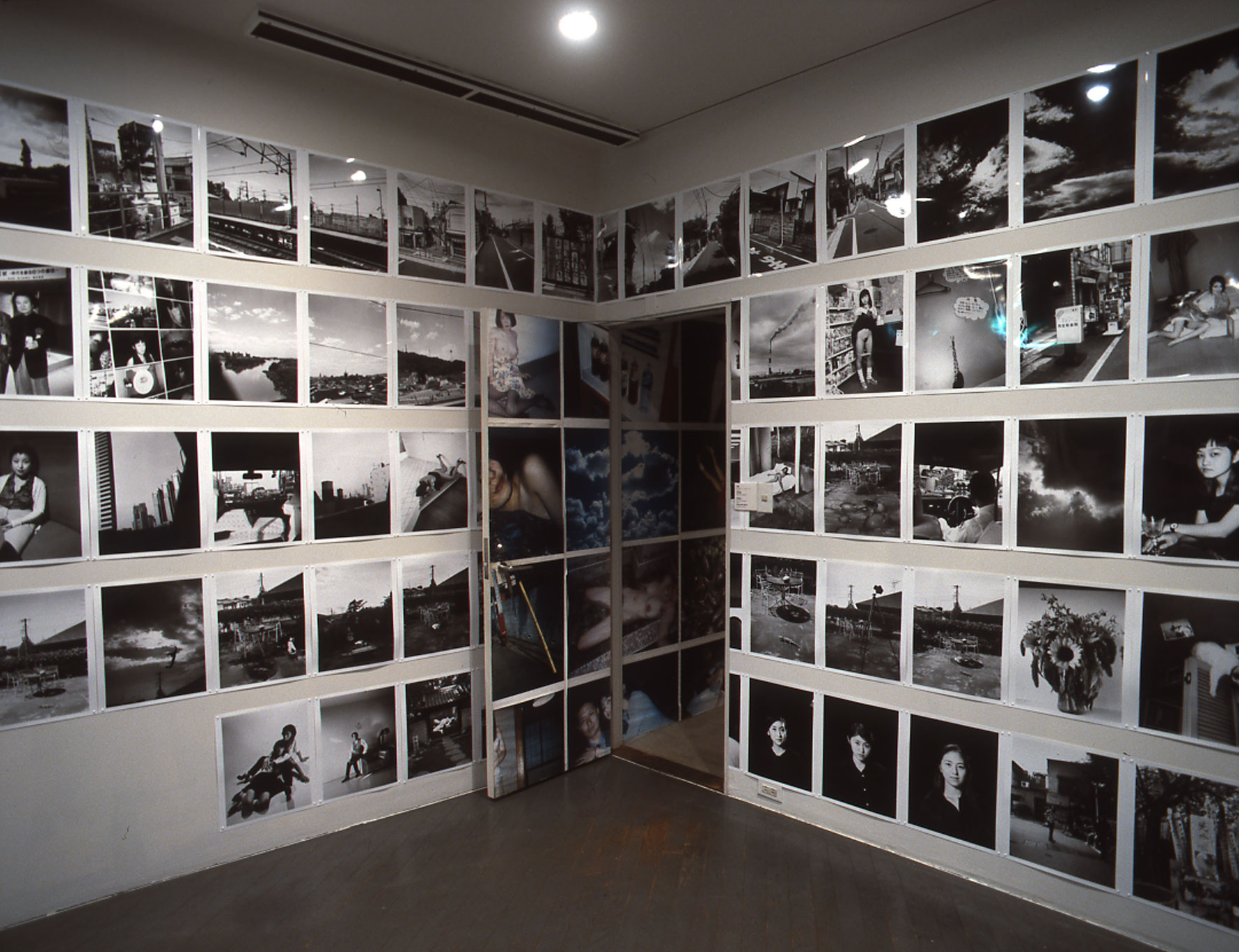 Photograph of one corner of a room, the walls and door tiled with photographs