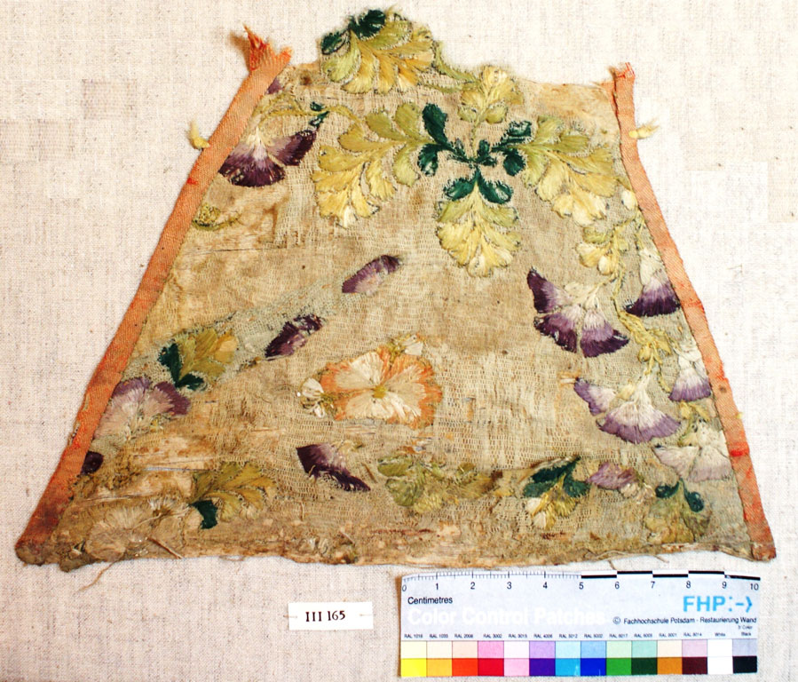 Tattered trapezoid (probably formerly a triangle) embroidered with purple and yellow flowers, orange ribbon edging