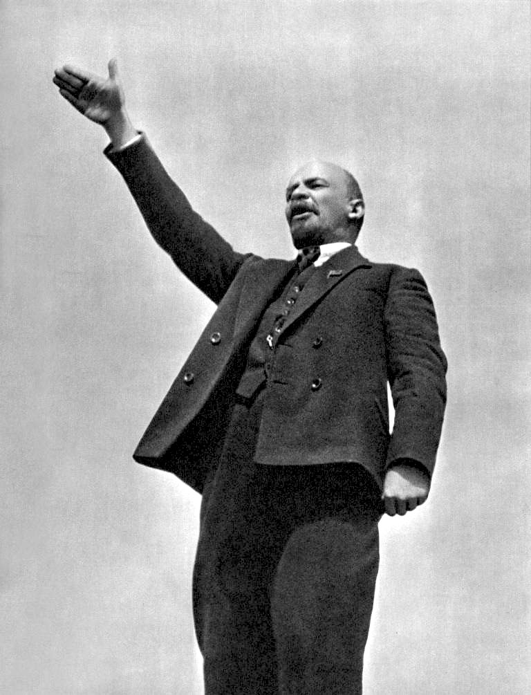 Photograph of Lenin standing, facing to the left with his right arm raised